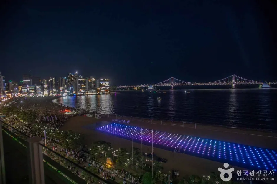 夜の広安里ビーチ、ライトアップされた広安大橋と砂浜の光る作品、そして大勢の人