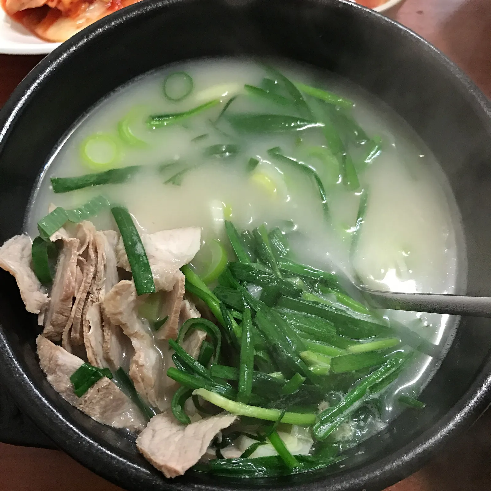 A stone bowl of dwaeji gukbap, milky pork broth with sliced pork and chives