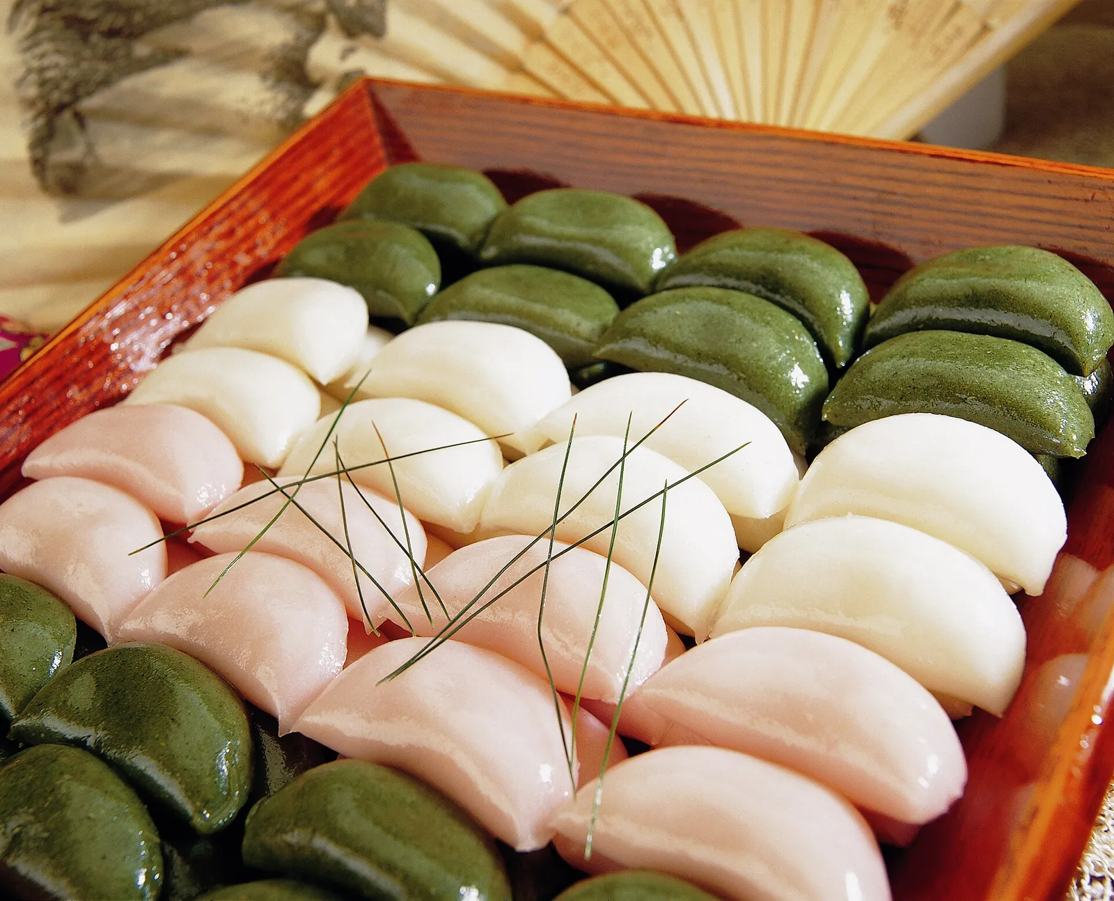 Rows of white, pink and mugwort-green songpyeon rice cakes in a wooden box, laid on pine needles