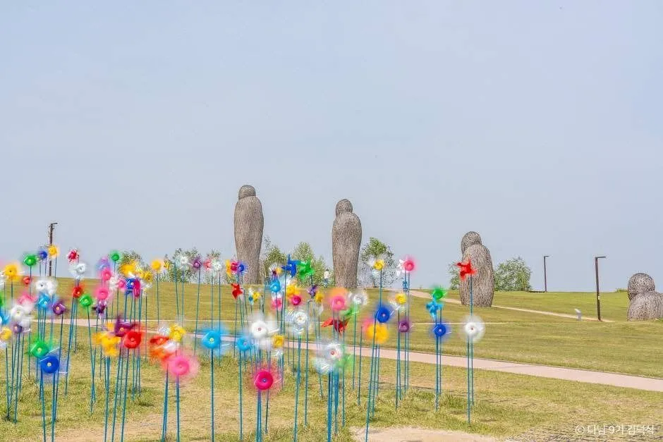 臨津閣平和ヌリの芝生の丘に並ぶ色とりどりの風車と、背後に立つ人型の彫刻