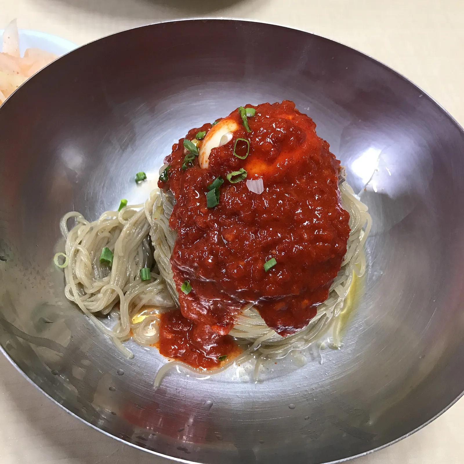 真鍮の器に盛られたビビン冷麺。細い麺の上に赤い薬味だれが山盛りにのっている
