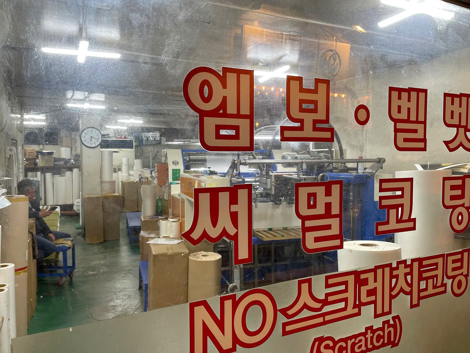 The window of a coating works, the jobs it takes painted in red lettering, machines and paper rolls inside
