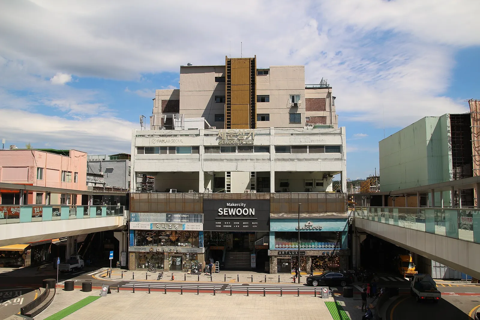 The front of Sewoon Sangga, lighting shops lined up beneath a Makercity SEWOON sign with the elevated walkway running out to either side