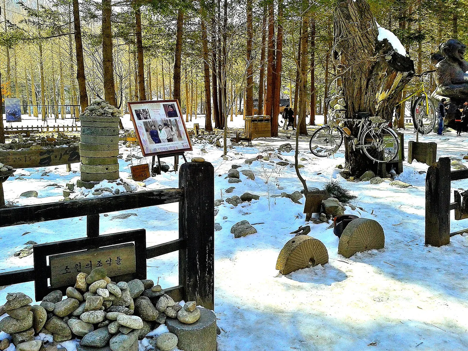 雪の南怡島、葉の落ちた木々の下に積み石と自転車が置かれた冬のソナタの記念展示