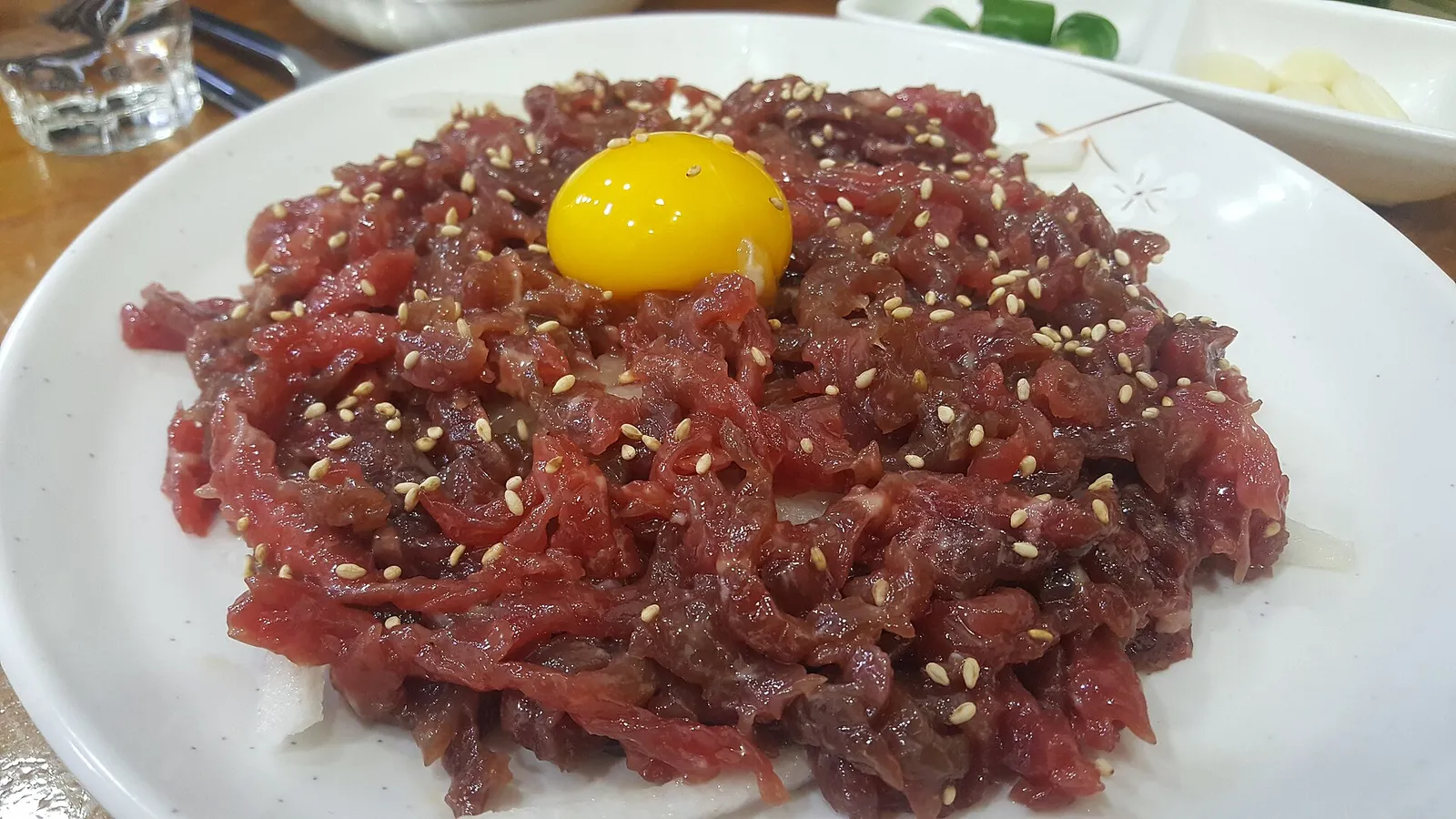 A plate of yukhoe topped with an egg yolk, served with garlic and green chilli on the side