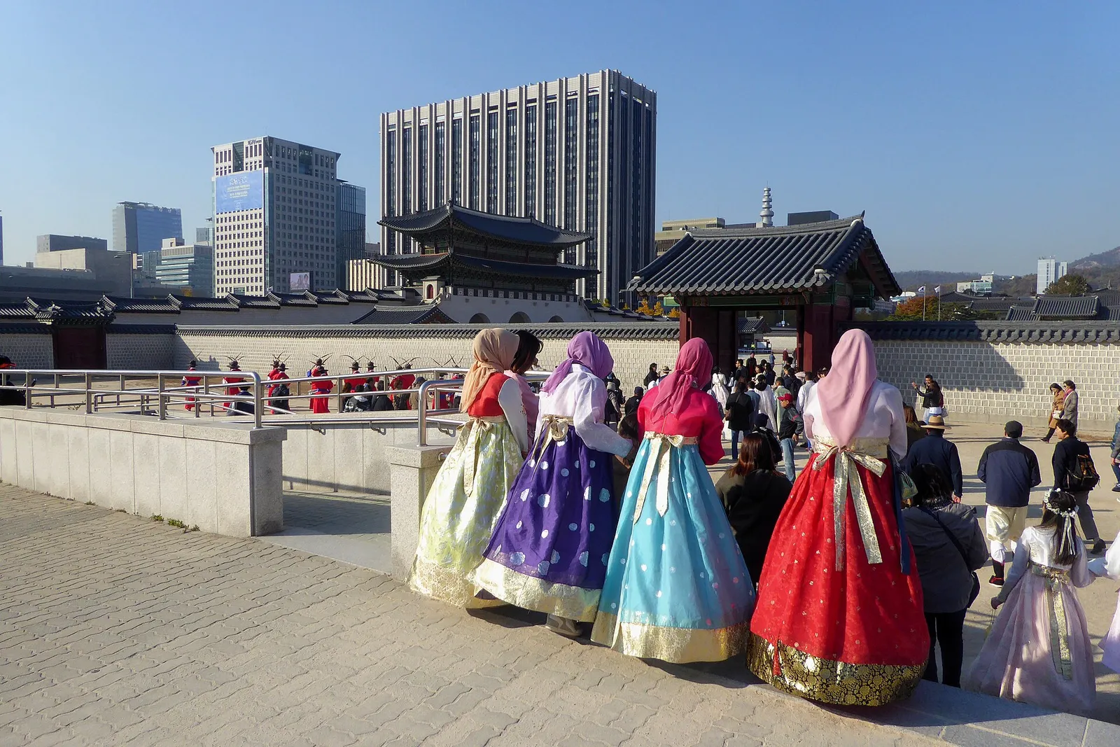 히잡을 쓰고 한복을 입은 네 사람이 경복궁 담장 너머 광화문과 수문장 행렬을 바라보고 있다