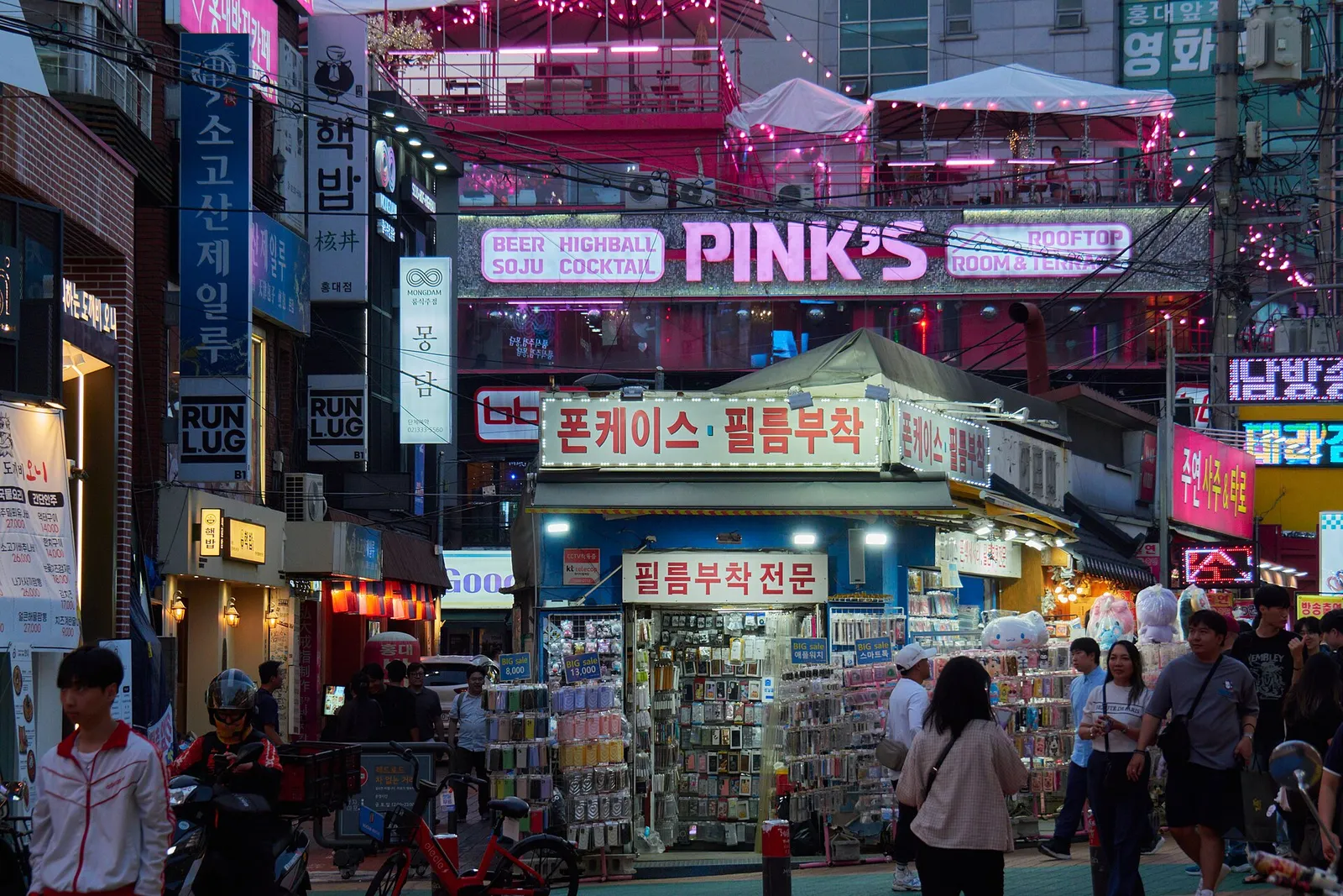 A Hongdae street at night lined with neon signs, shops and pedestrians