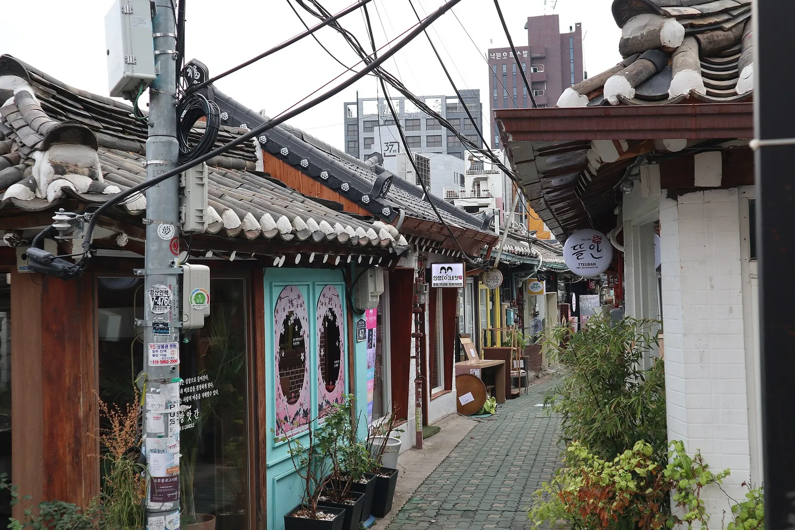 A narrow Ikseon-dong alley, power lines tangled above the tiled hanok roofs on either side and an officetel block rising behind