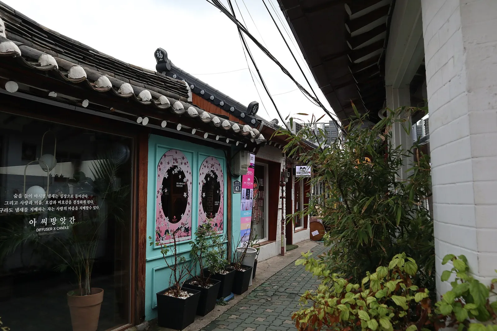 Shops with mint-green wooden doors and glass fronts running along a narrow alley beneath tiled hanok eaves