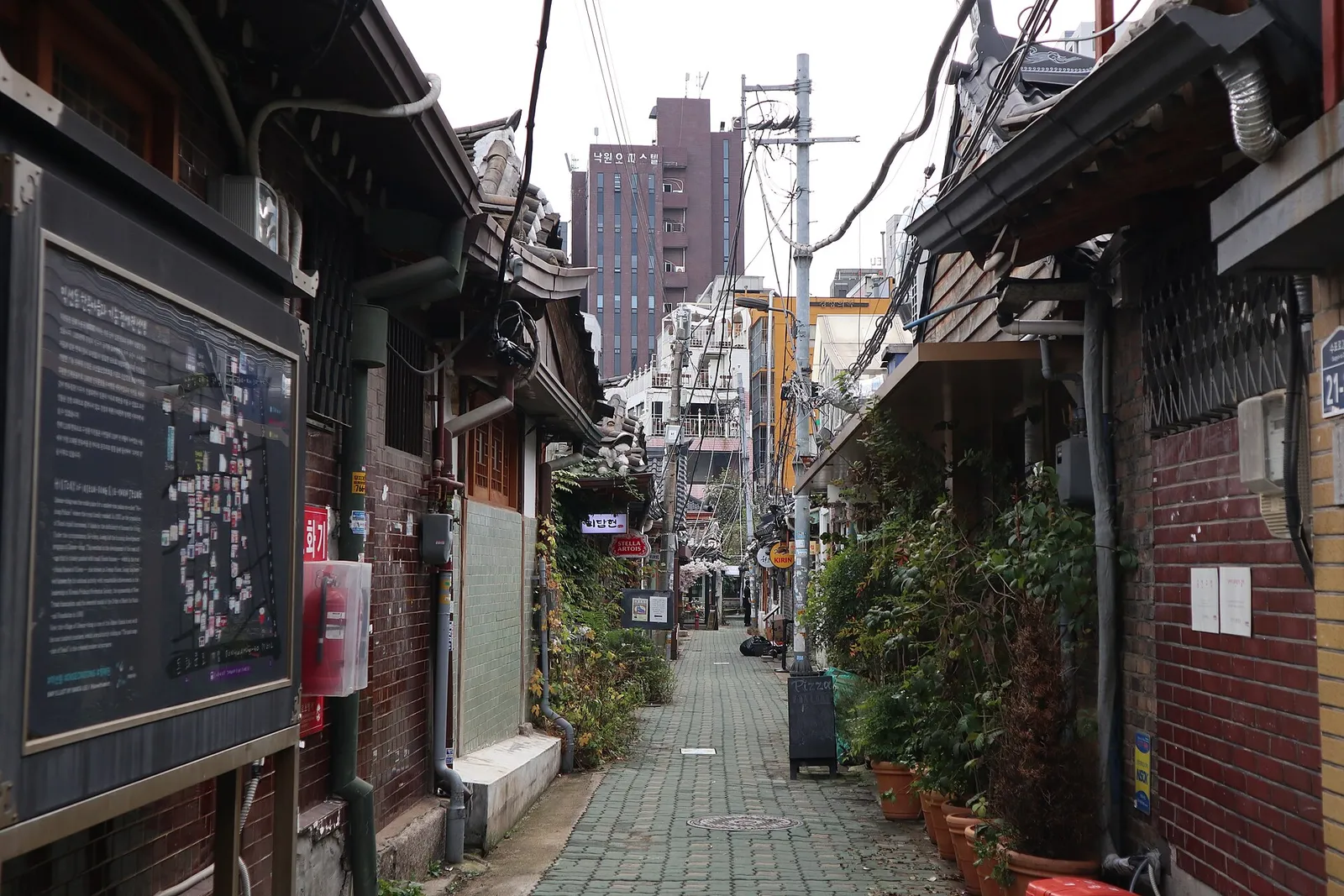 An information board at the entrance to an Ikseon-dong alley, with hanok eaves and shopfronts running on beyond it