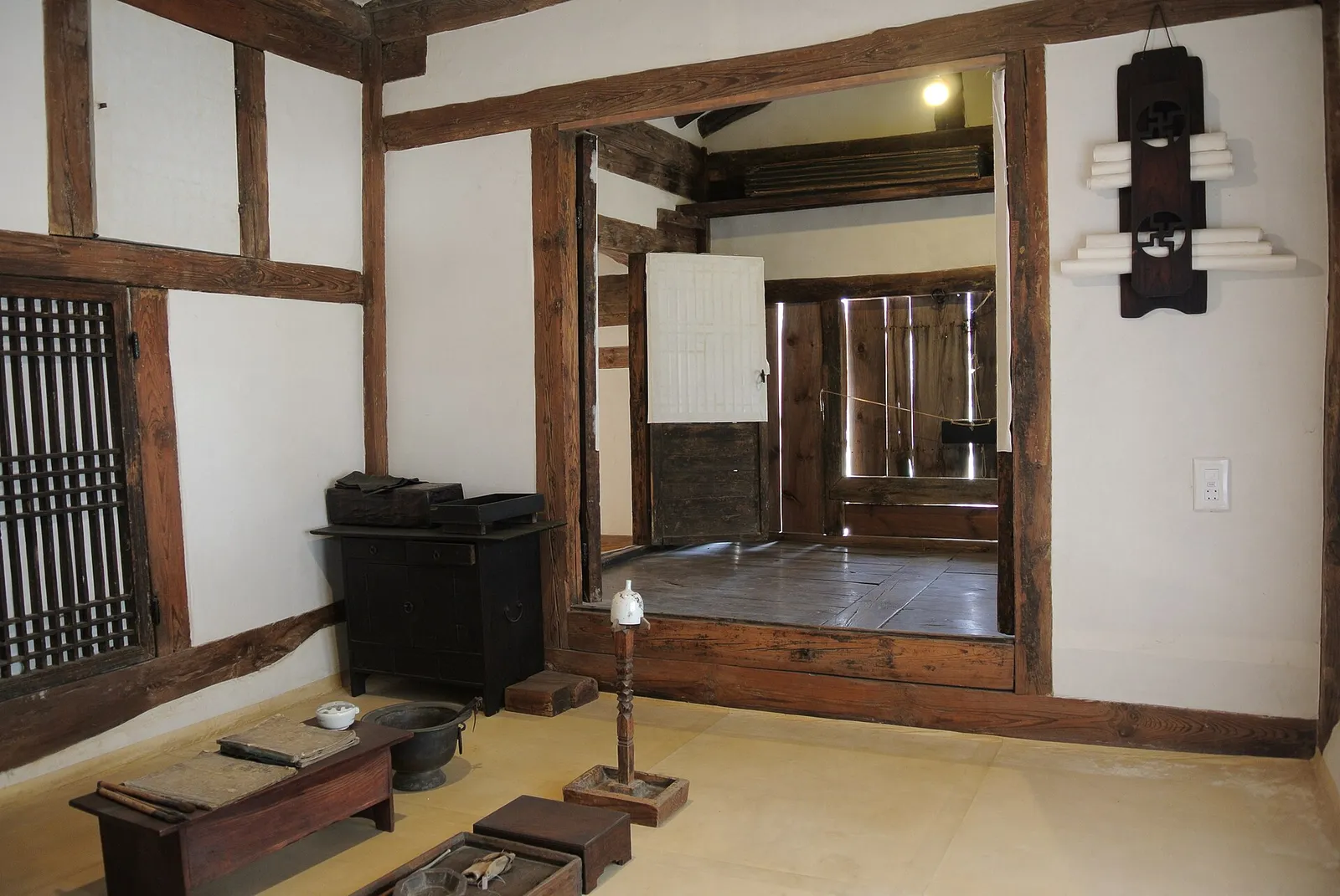 Inside a hanok room, the wooden floor visible between paper-screen doors and timber posts