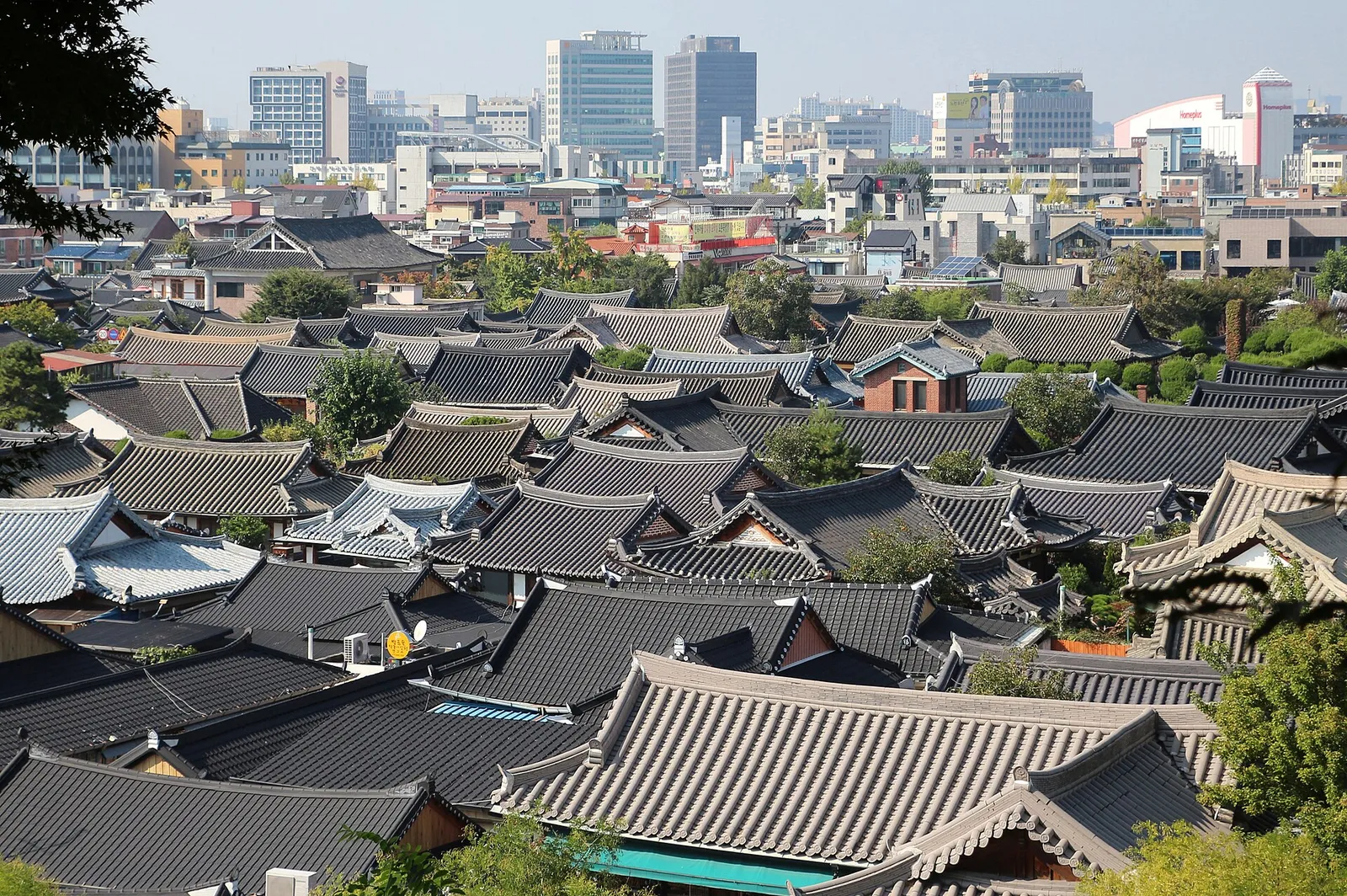 Rows of curved tiled hanok roofs filling the foreground with modern office towers behind them