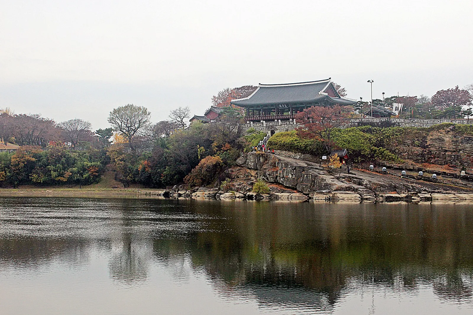 南江の対岸から見た矗石楼。岩の崖の上の城壁にのった楼閣と、紅葉した木々