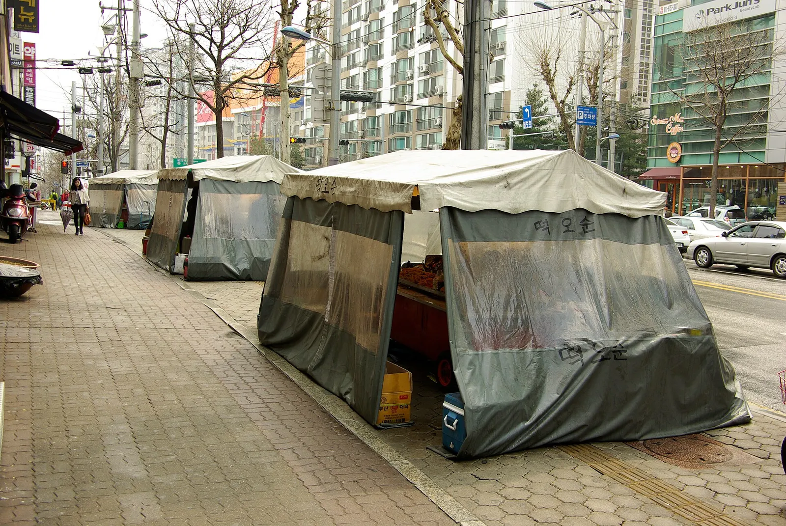 A row of street tent bars covered up during the day, with the pavement running alongside