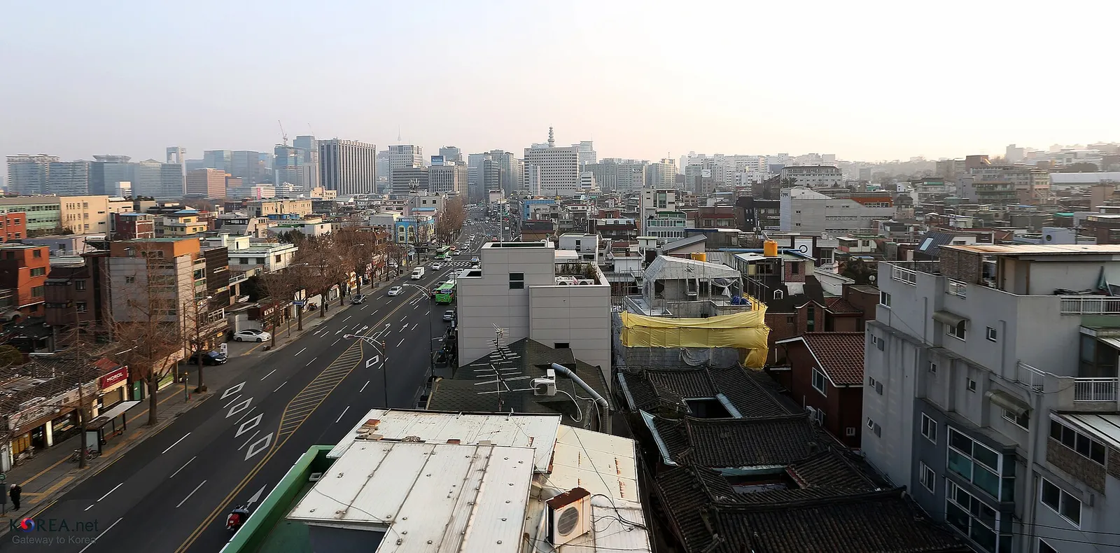 Seochon seen from a rooftop, low tiled roofs running on and the tall towers of the city centre in the distance