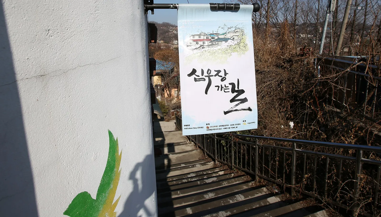 「尋牛荘へ行く道」の横断幕が掛かった急な階段。その向こうの丘に家々がびっしりと建ち並んでいる