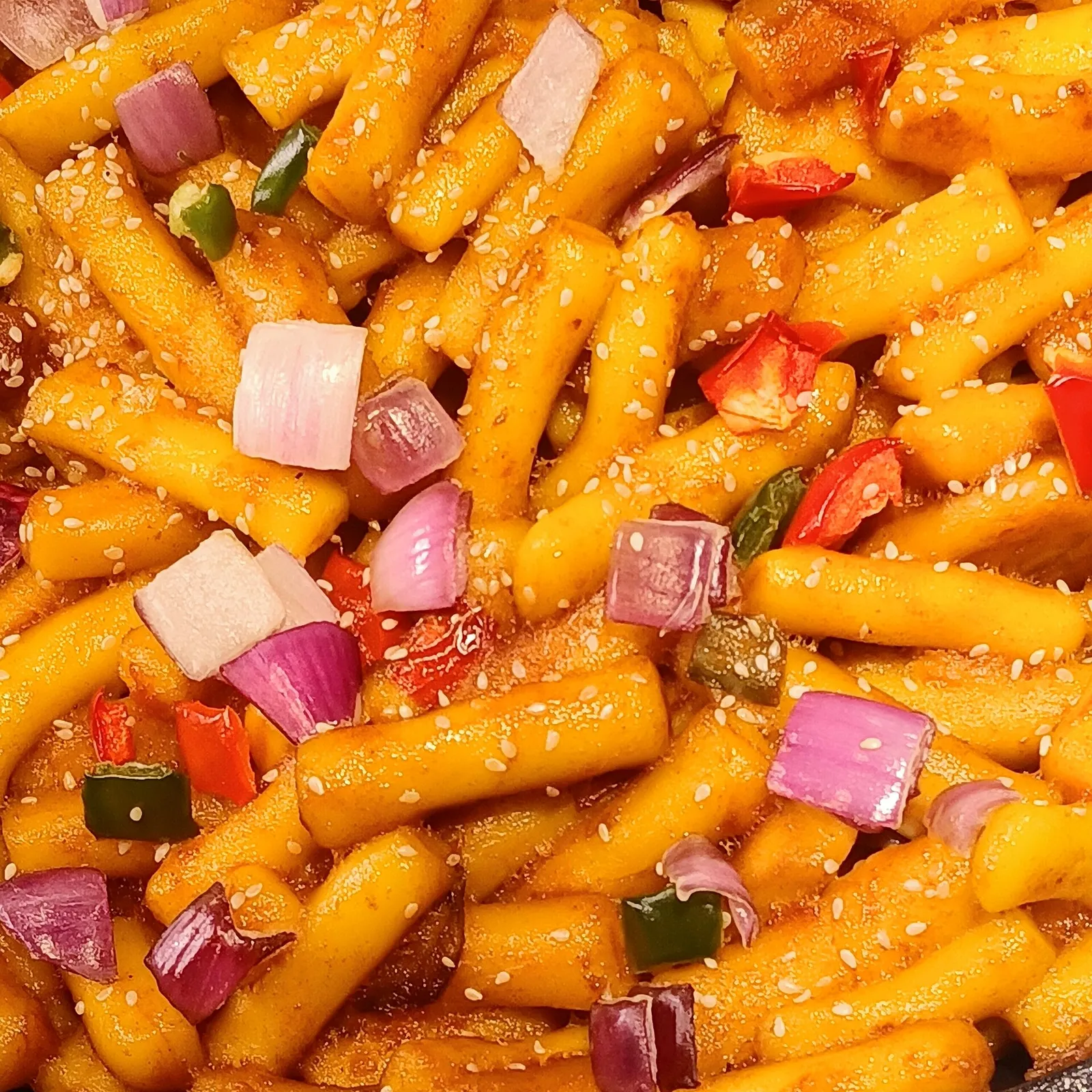 A close-up of stir-fried tteokbokki topped with onion, chilli and sesame seeds