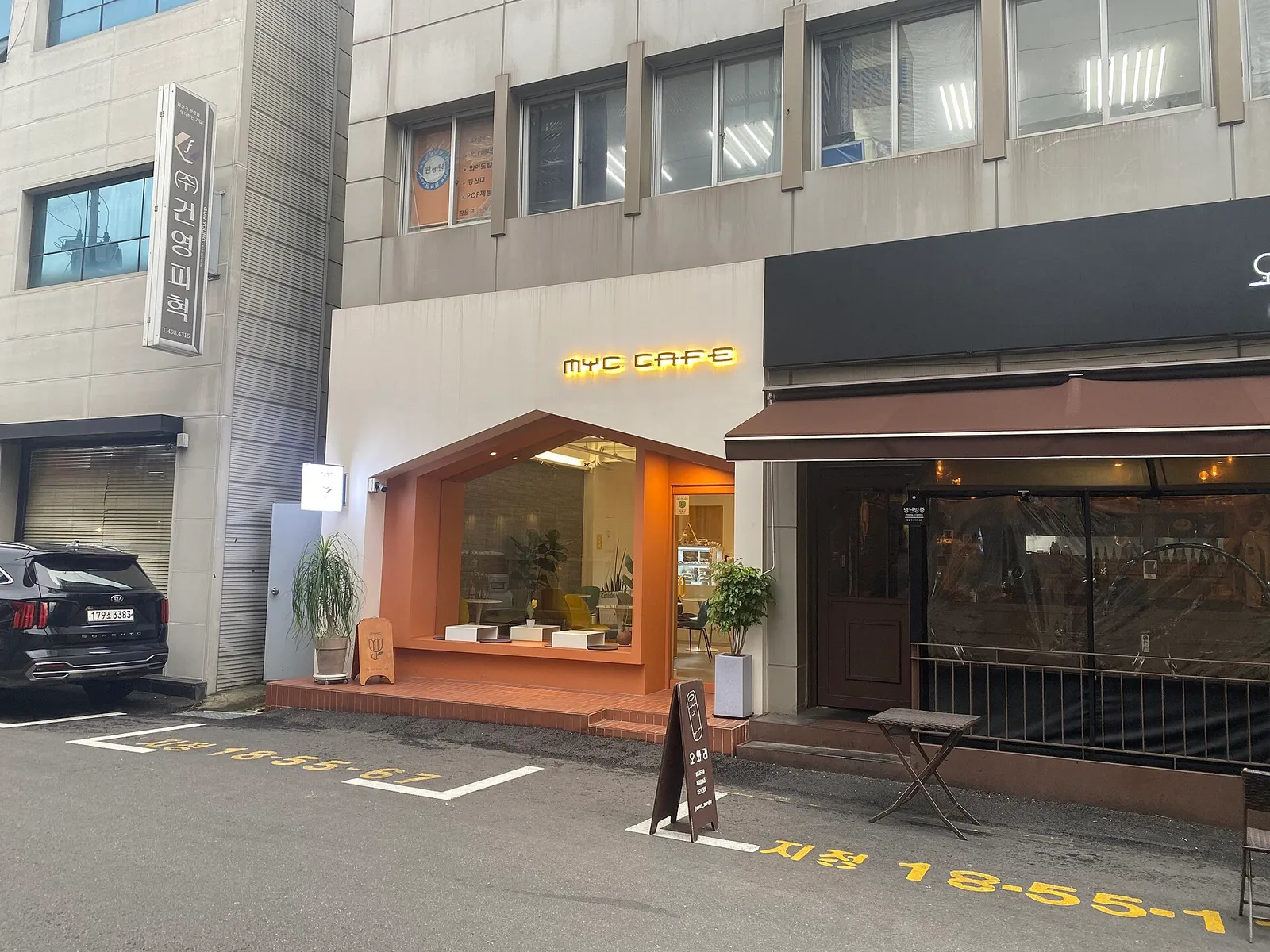 The orange entrance of a small cafe standing right beside a leather factory sign