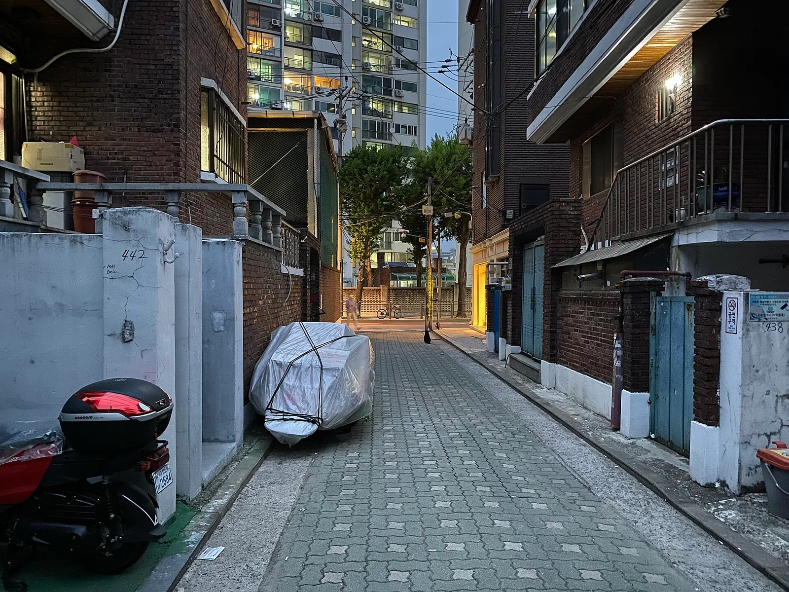 赤レンガの住宅の間を抜ける細い路地、その先に明かりのついた新しい高層マンションが立っている